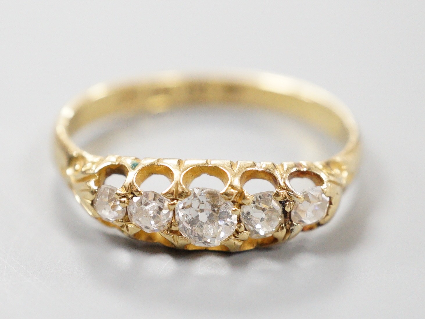 A late Victorian 18ct gold and graduated claw set five stone diamond half hoop ring, size N, gross weight 2.5 grams.